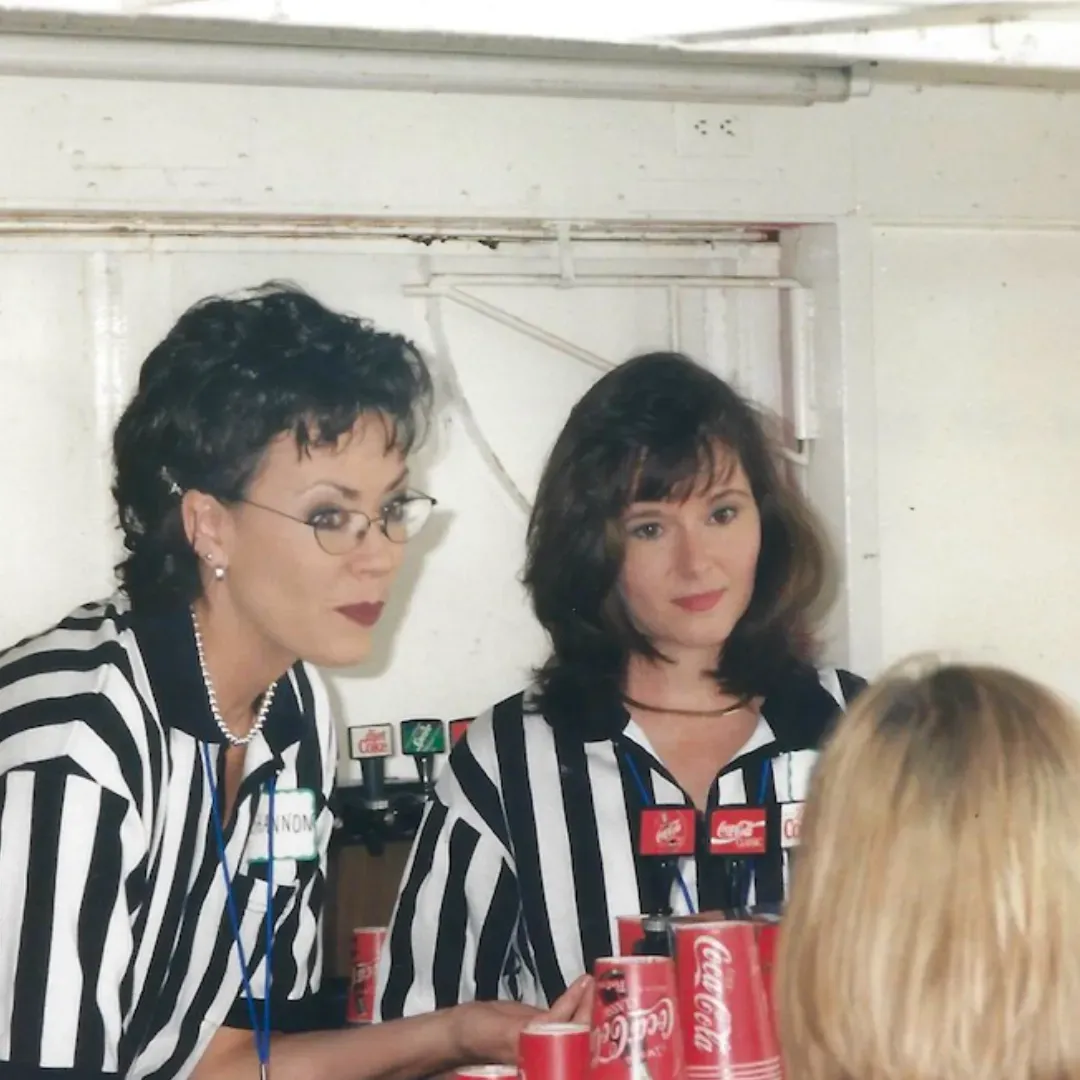 Two women sitting at a table with coca cola cans
