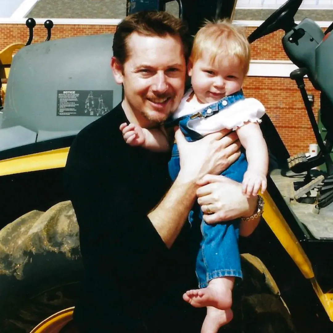 A man is holding a baby in front of a tractor