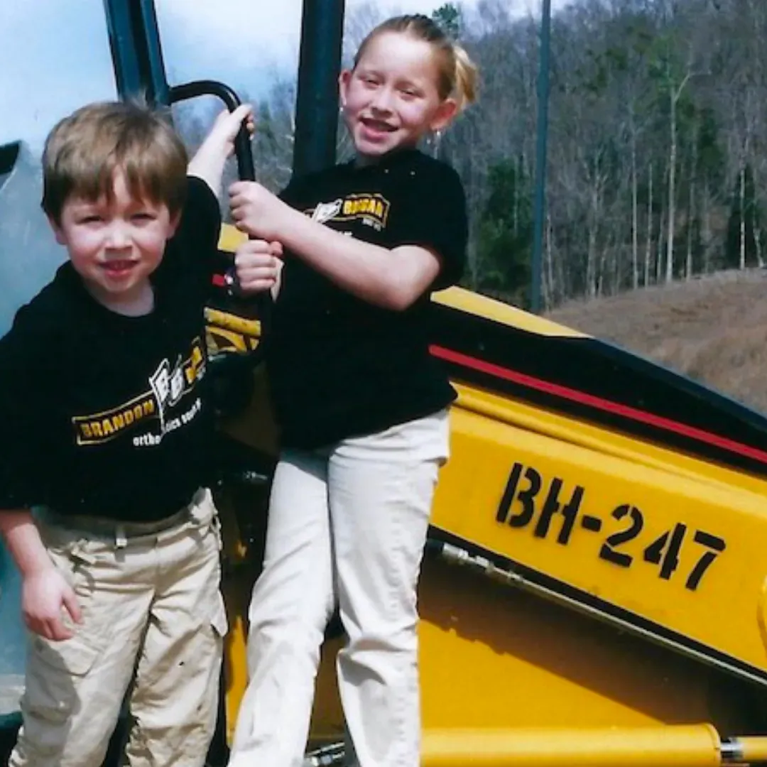 A boy and a girl are standing next to a yellow vehicle with bh-247 on it