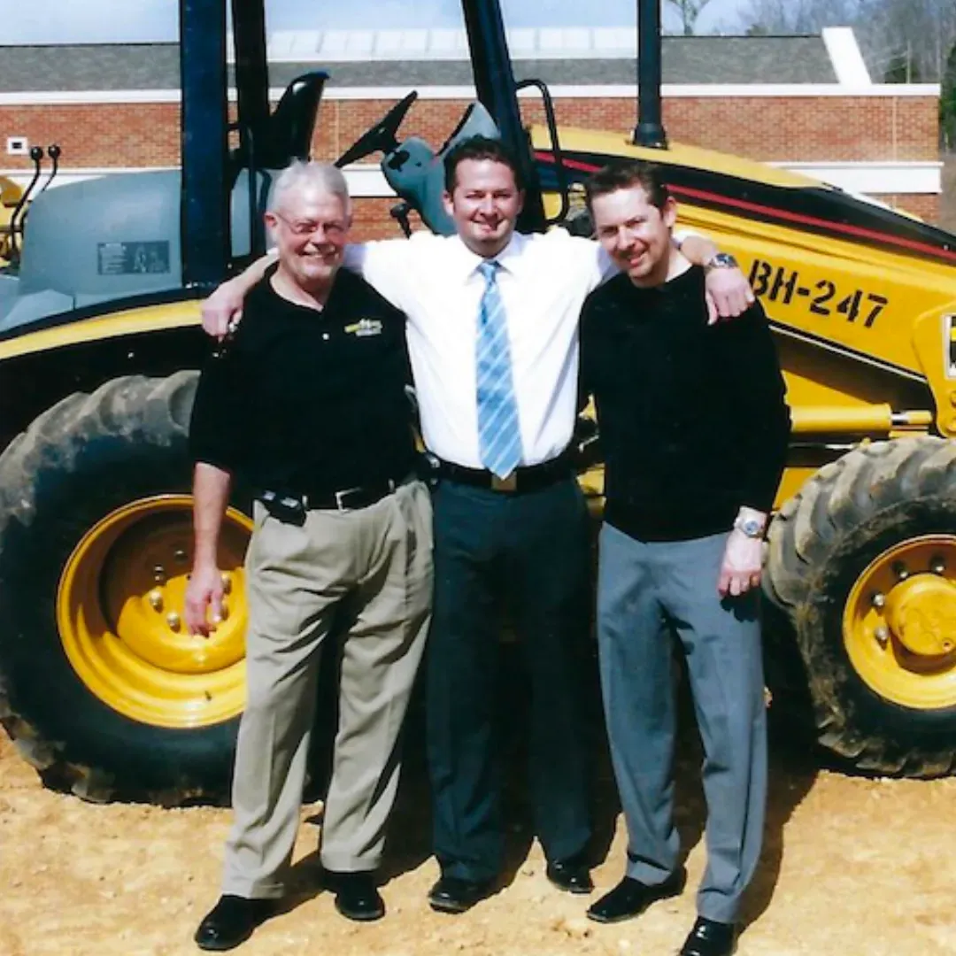 Three men pose for a picture in front of a bh-247 tractor