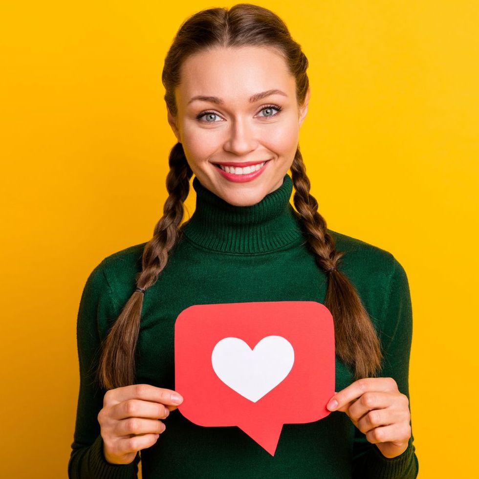 A woman is holding a red speech bubble with a heart in it.