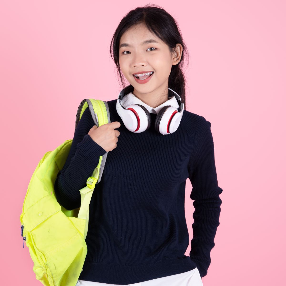 A young girl wearing headphones and carrying a yellow backpack