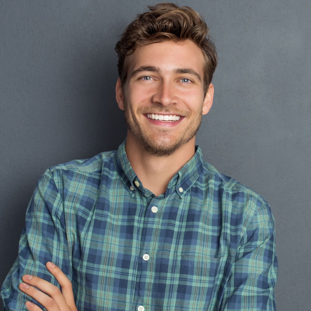 A man in a plaid shirt is smiling with his arms crossed.