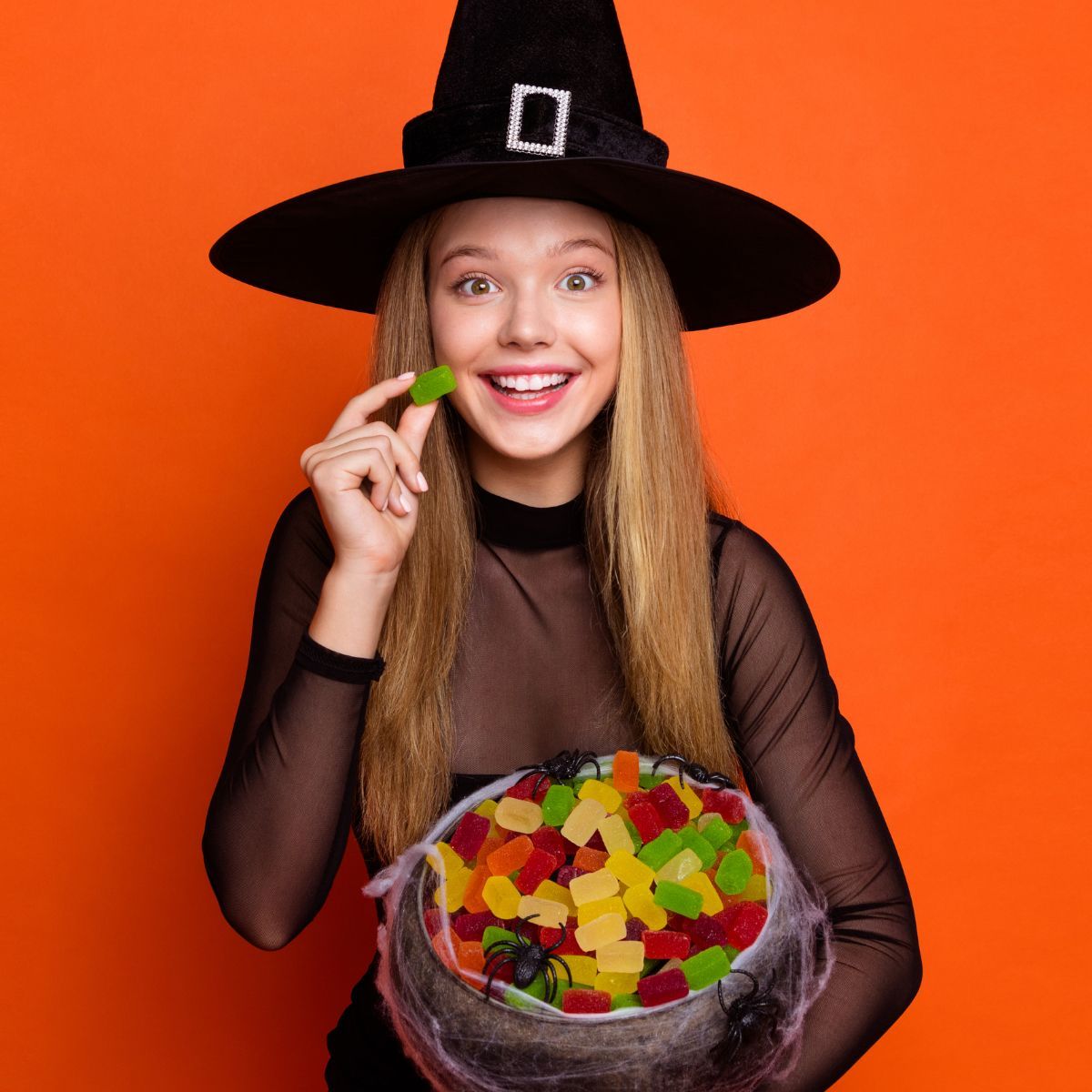 A woman in a witch hat is holding a bowl of gummy bears.