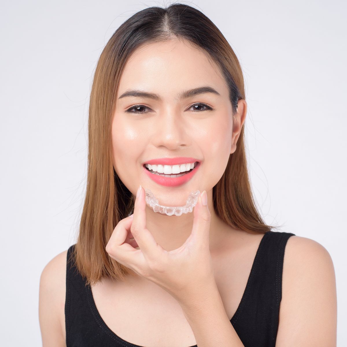 A woman is smiling while holding a clear brace on her teeth.