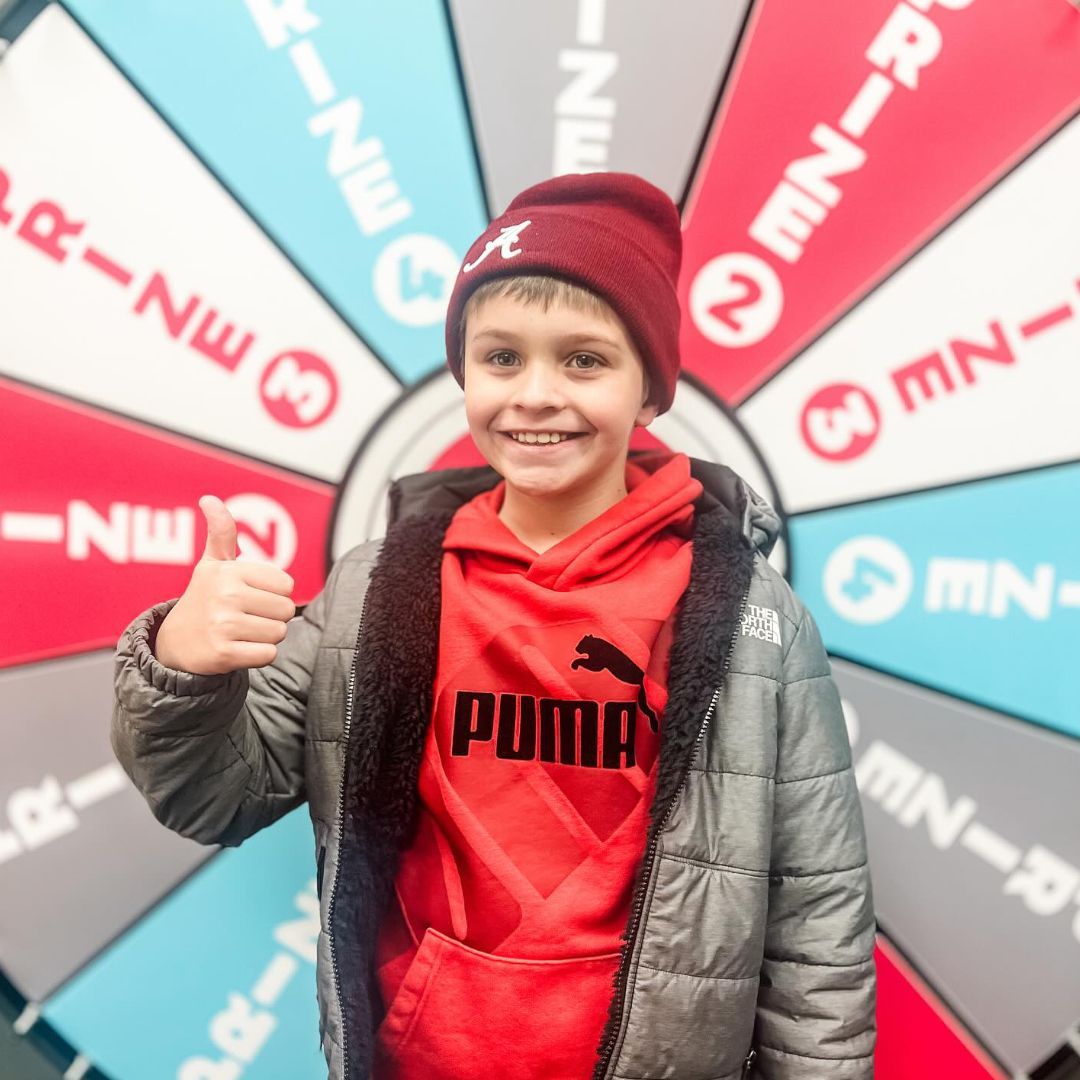 A young boy wearing a red puma sweatshirt giving a thumbs up