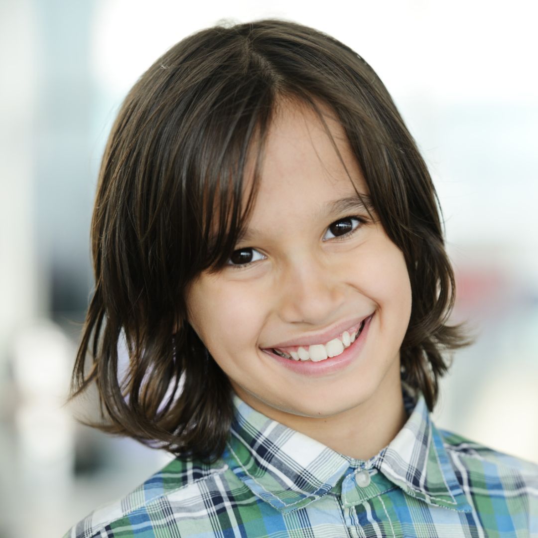A young boy wearing a plaid shirt smiles for the camera