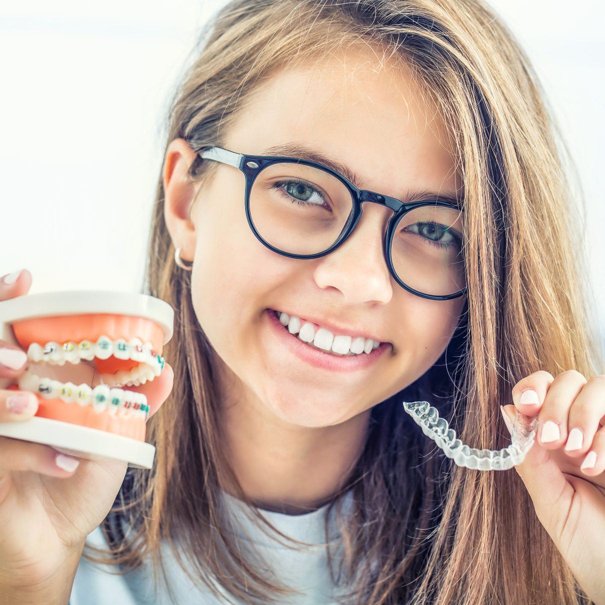 Teenage girl holding an example of braces and invisalign