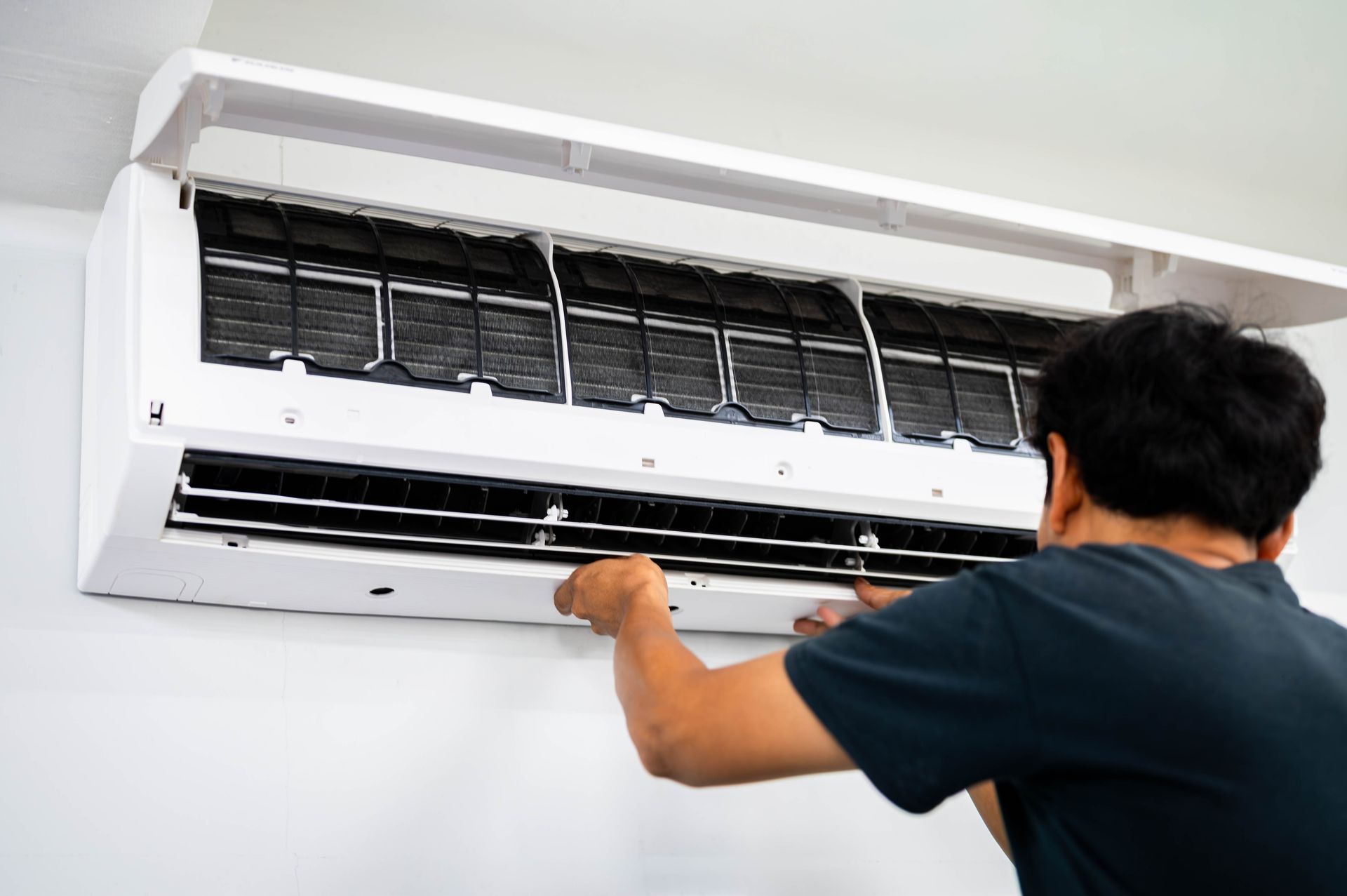 Man servicing an air conditioner; he is removing the air filters indoors.