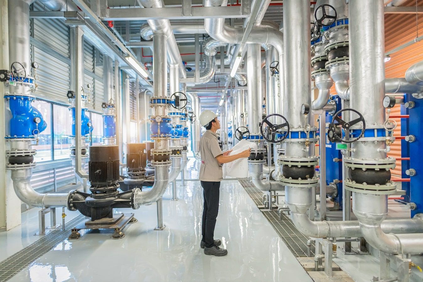 A man is standing in a factory looking at a blueprint.