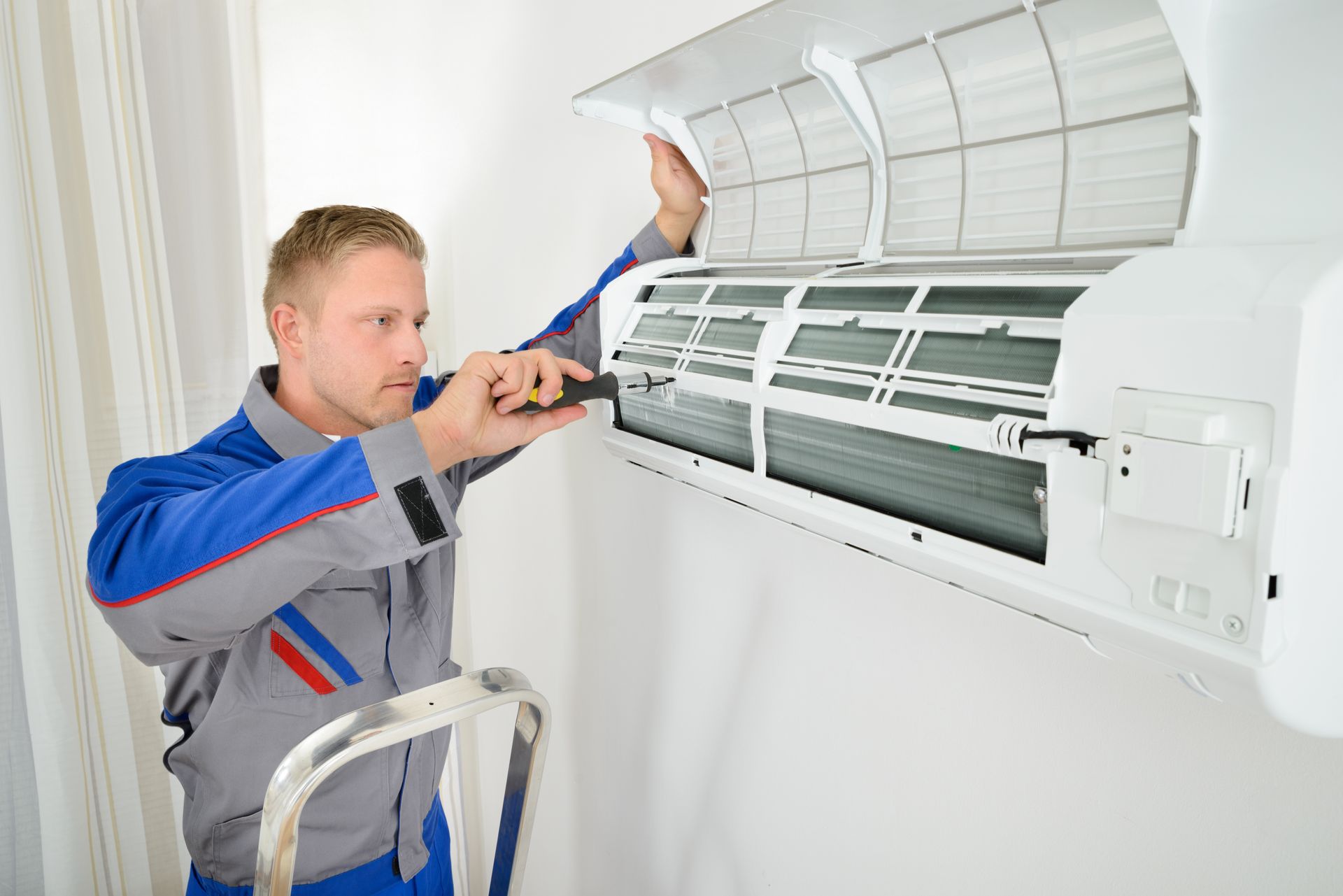 A man is fixing an air conditioner with a screwdriver.
