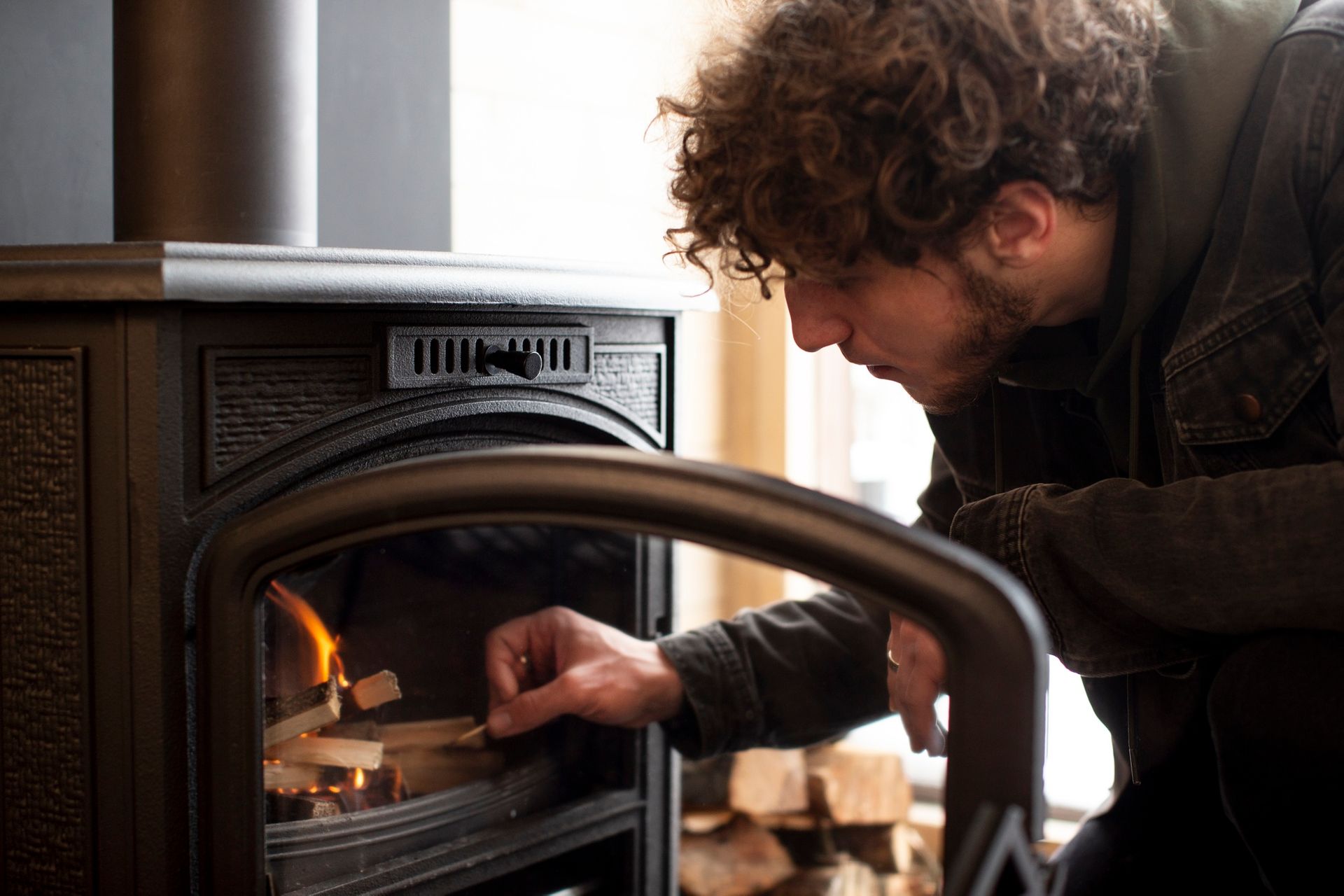 A man is opening the door of a wood stove.