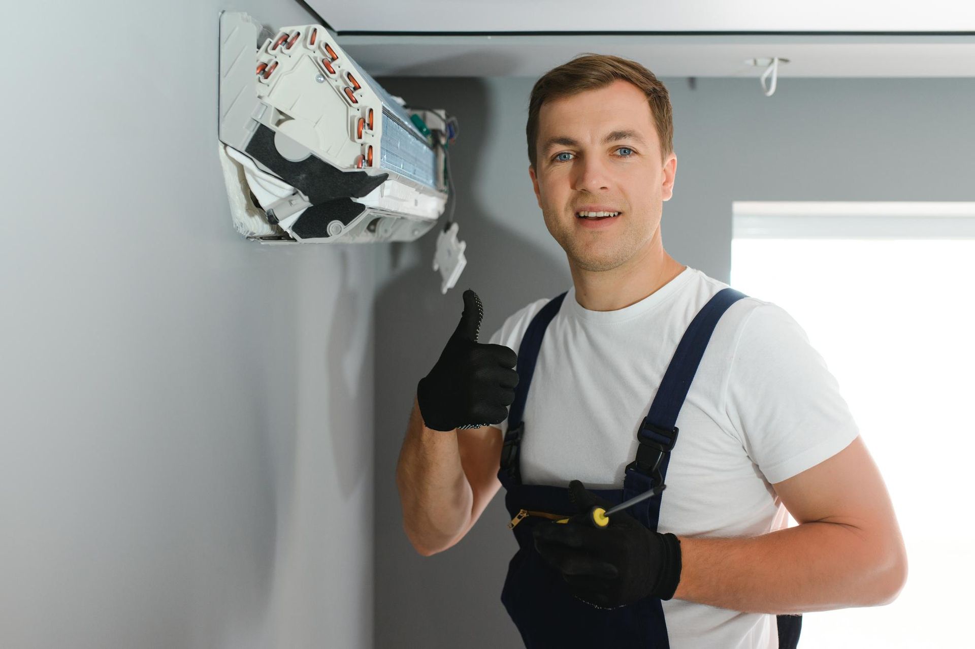 A man is fixing an air conditioner on the wall and giving a thumbs up.