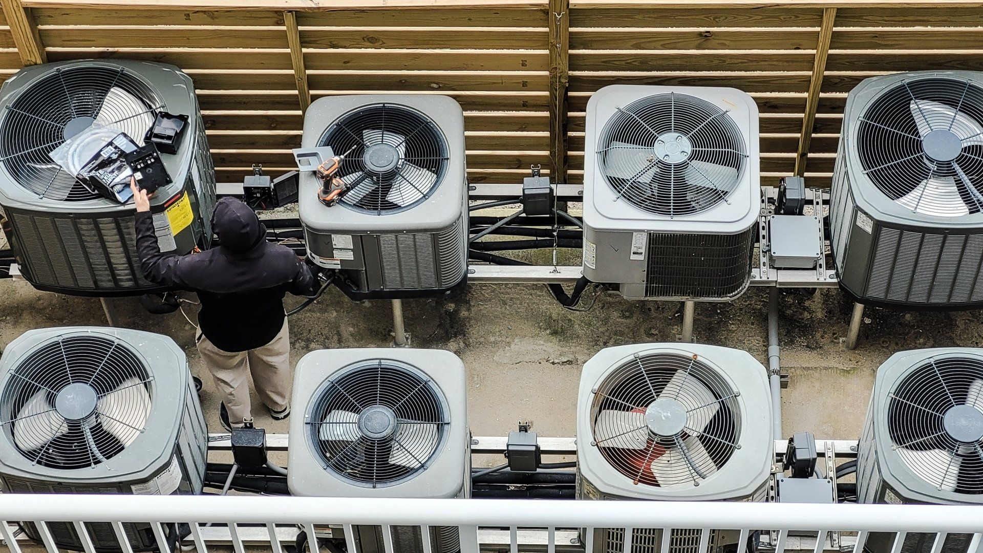 technician standing with multiple outdoor heating and cooling fan units
