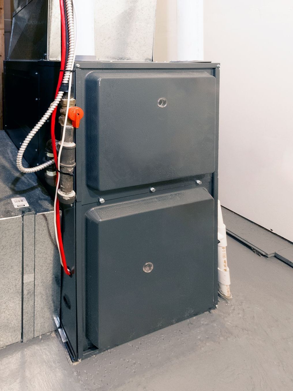 A large gray furnace is sitting in a room next to a wall.