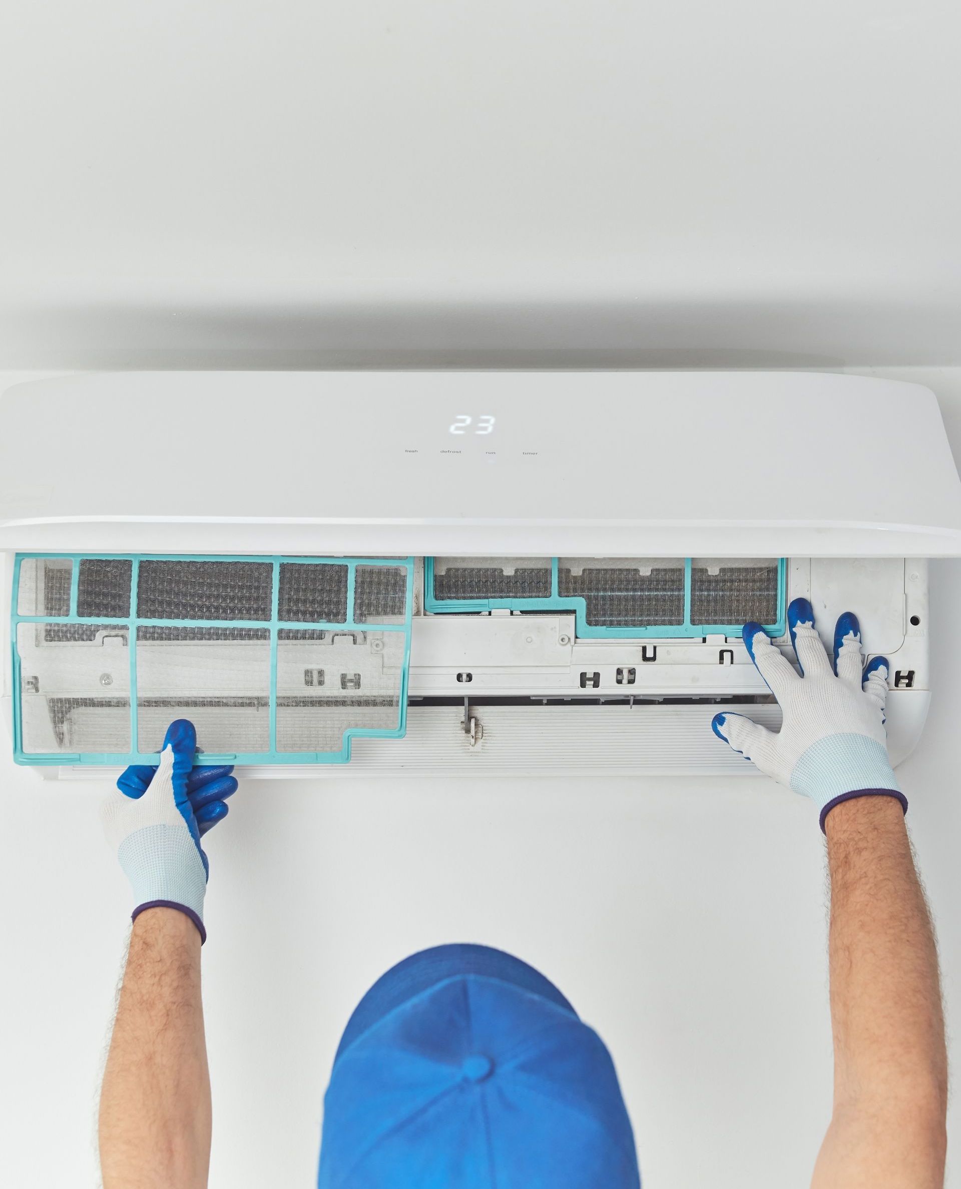 A man in a blue hat is cleaning an air conditioner.