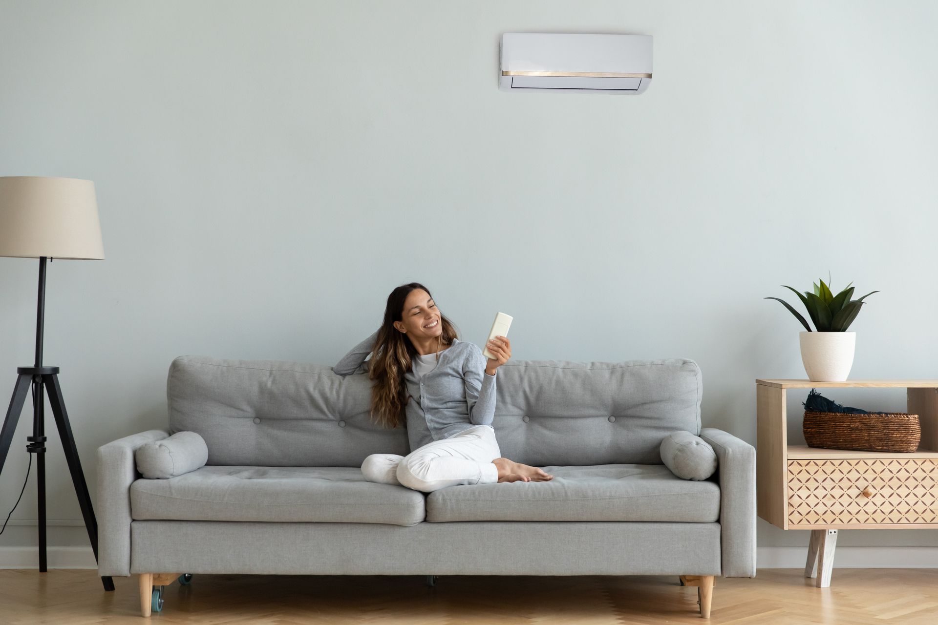 A woman is sitting on a couch in a living room holding a remote control.