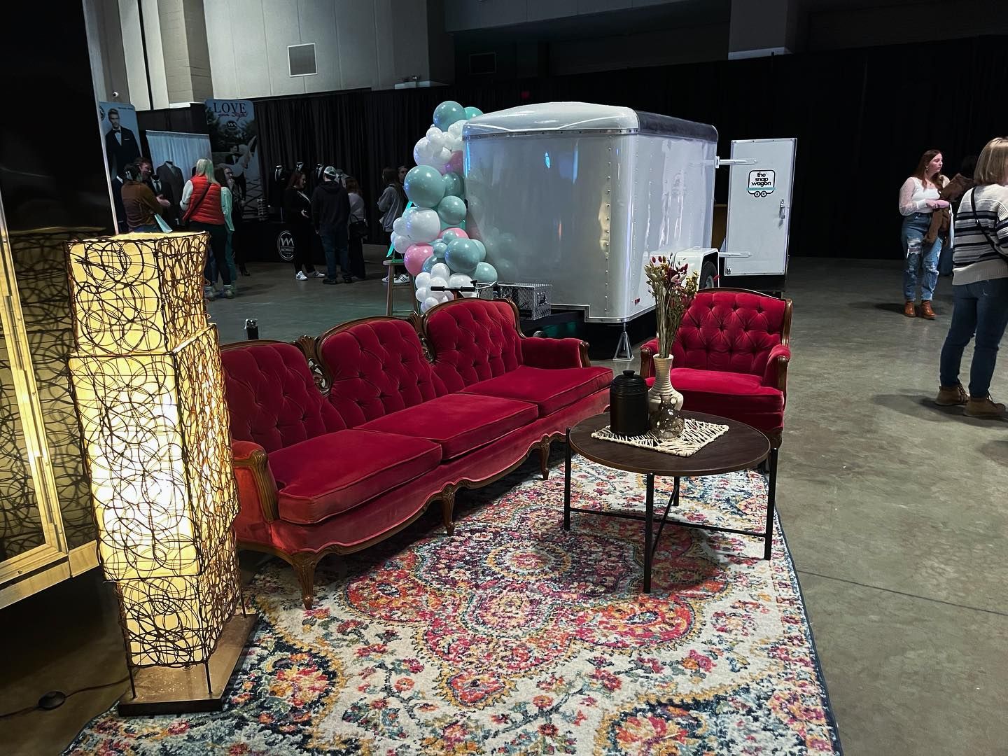 Red velvet sofa and chair on patterned rug, with a small table, in an event space.