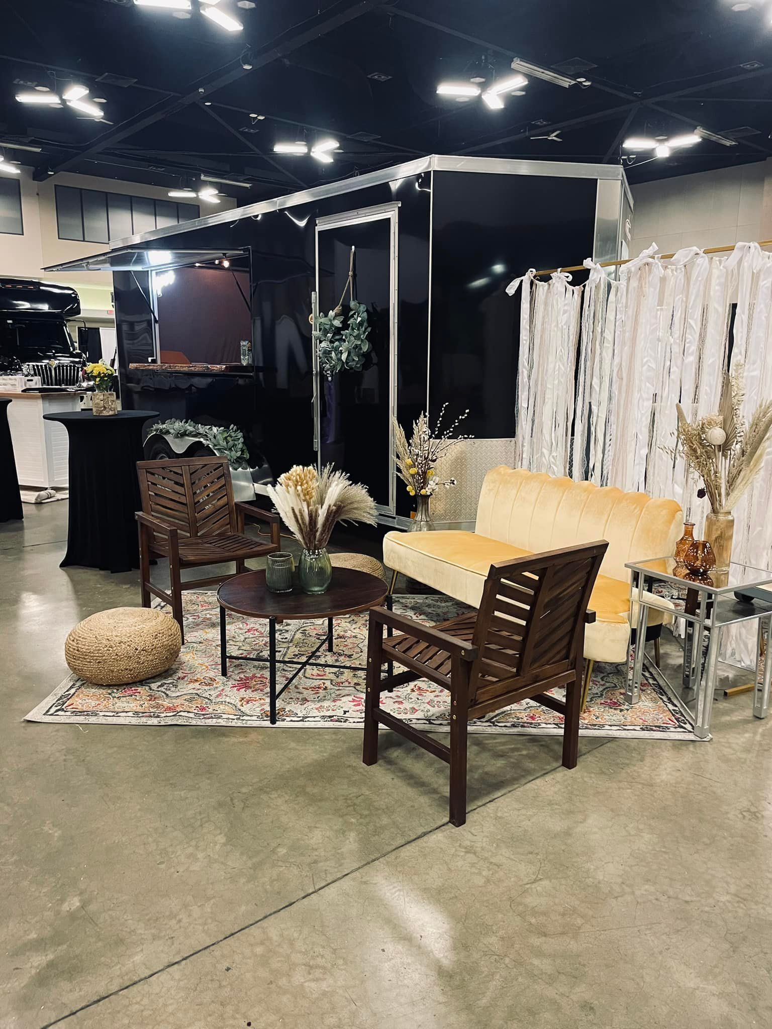Lounge area with black backdrop, sofa, chairs, rug, coffee table, and dried plants.