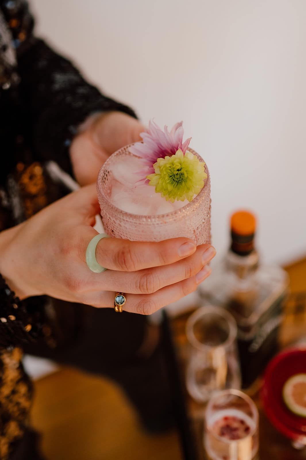 Person holds pink cocktail with flower garnish. Salt rim, ring, and bar setting.
