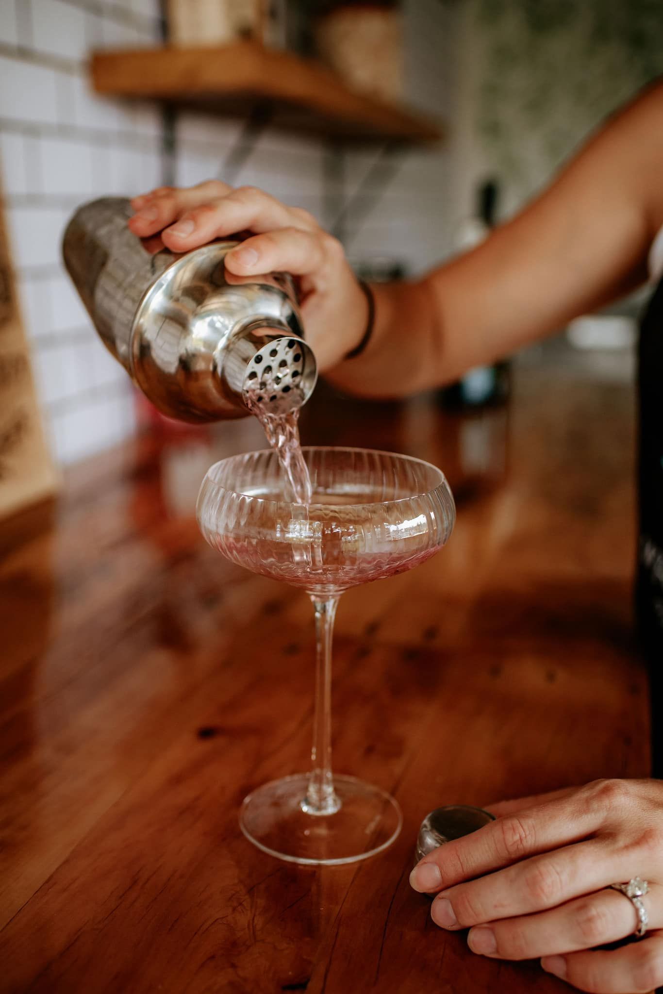Person pouring pink drink from shaker into stemmed glass.