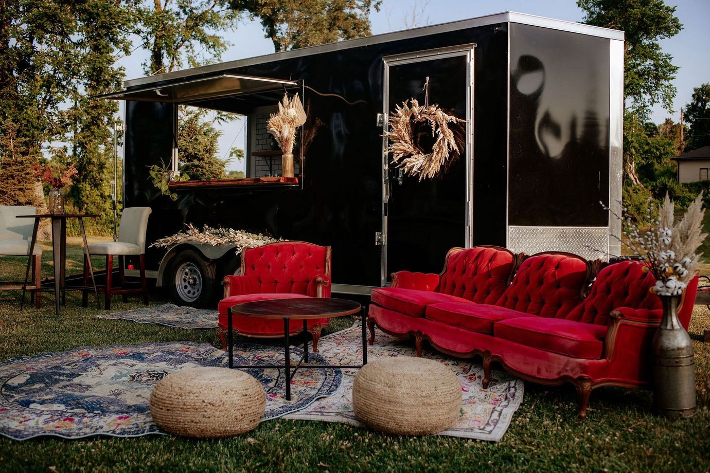 Black trailer bar with red velvet furniture and rugs in an outdoor setting.