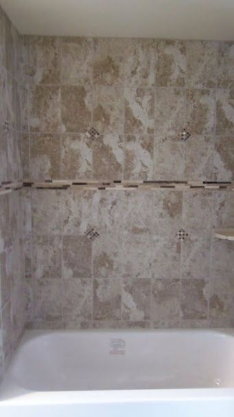A bathtub in a bathroom with tiled walls and shelves.