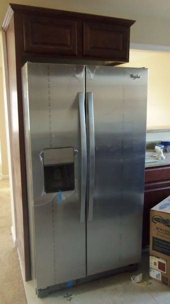 A stainless steel refrigerator is sitting in a kitchen next to a box.