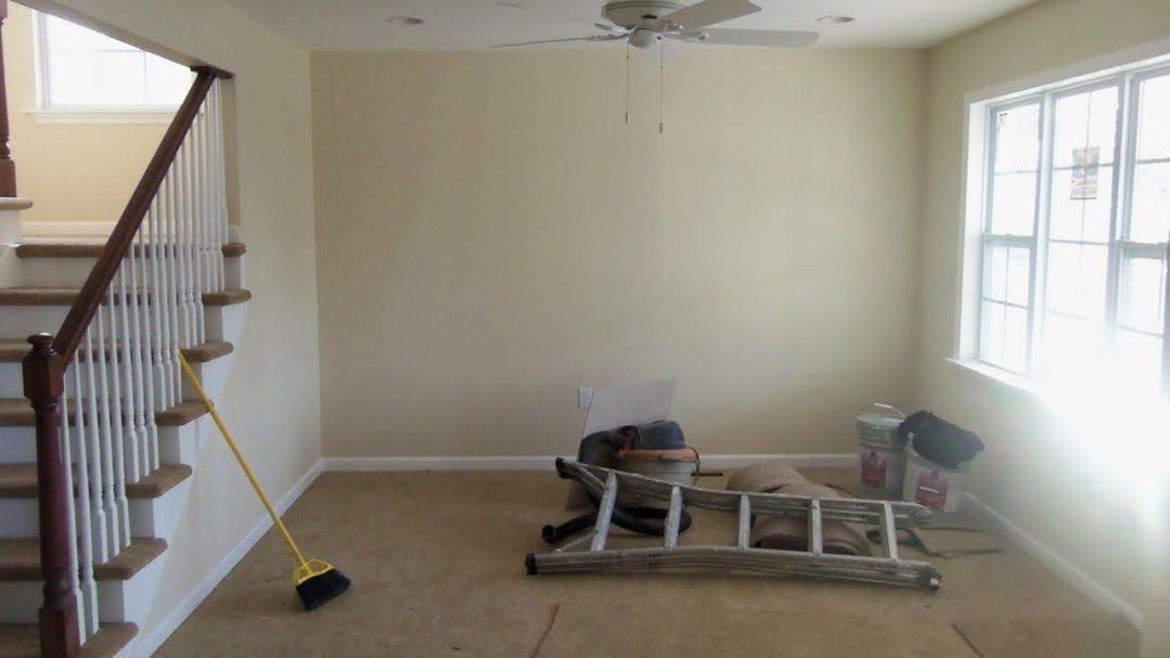 An empty living room with stairs , a ladder , and a broom.