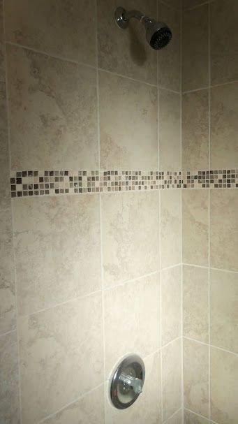A shower with a shower head and a mosaic border on the wall.