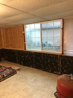 Basement interior with a window and weathered walls. There's a rug, blinds, and a red object.