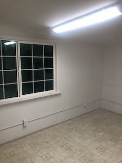 Empty room with window, white walls, linoleum floor, and fluorescent lighting.