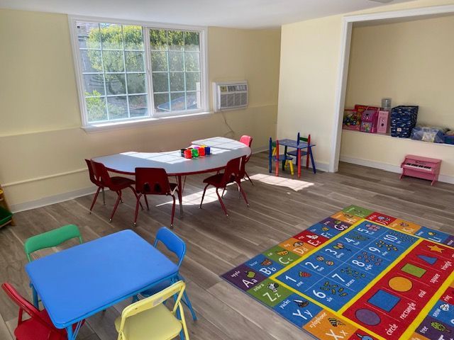Playroom with tables, chairs, a rug, and a window.