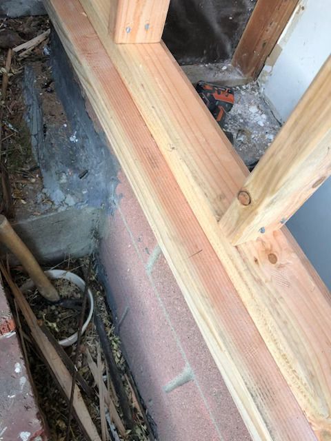 New wooden framing installed on a brick foundation next to a dirt area with tools.