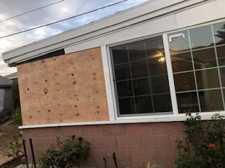 A house with a boarded-up window and a broken window; exterior view.