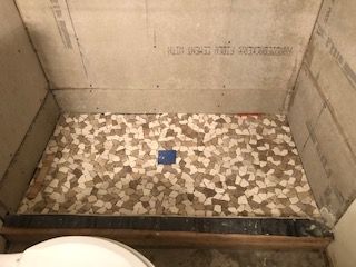 Shower stall with mosaic tile floor, unfinished walls, and a blue drain cover.