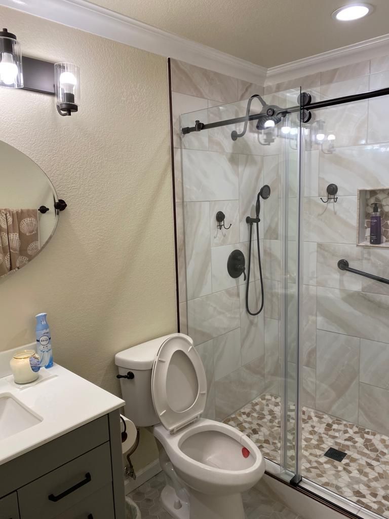 Bathroom with shower, toilet, vanity. Light beige walls, white tile, gray vanity, glass shower door.