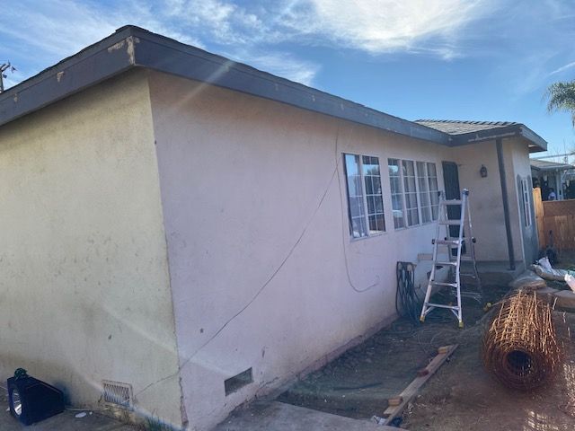 Beige house with a ladder in front of the windows on a sunny day.