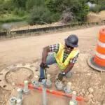 Construction worker in yellow vest, kneeling on a road, working on metal.