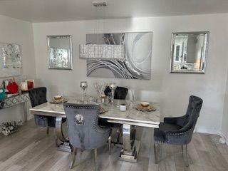 Dining room with white walls, marble table, velvet chairs, silver accents, and abstract art.
