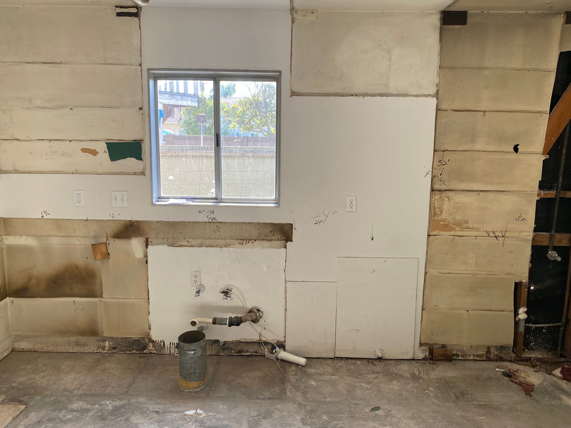 Kitchen wall gutted during renovation with window and exposed plumbing.