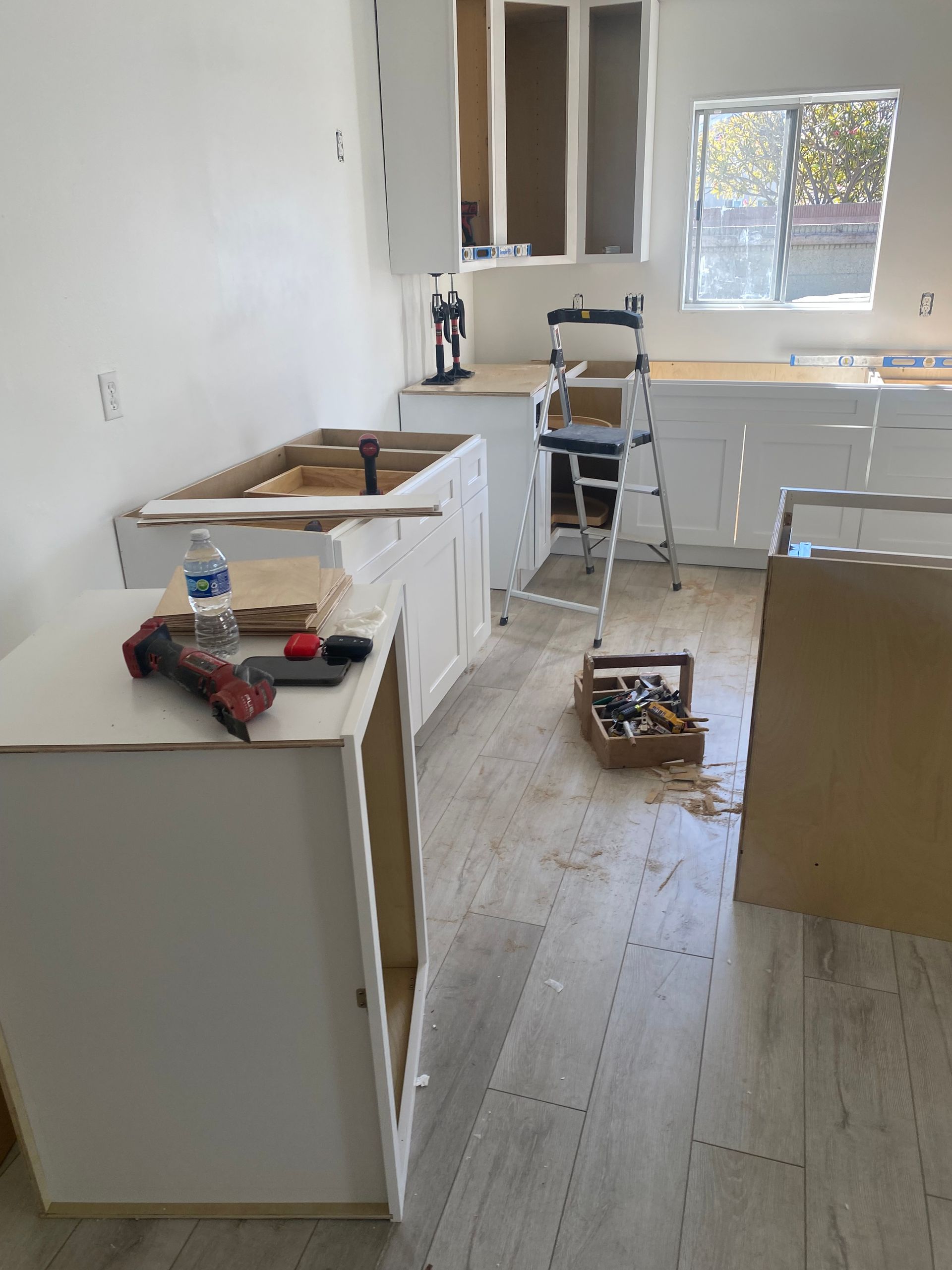 Kitchen under construction with white cabinets and tools scattered.