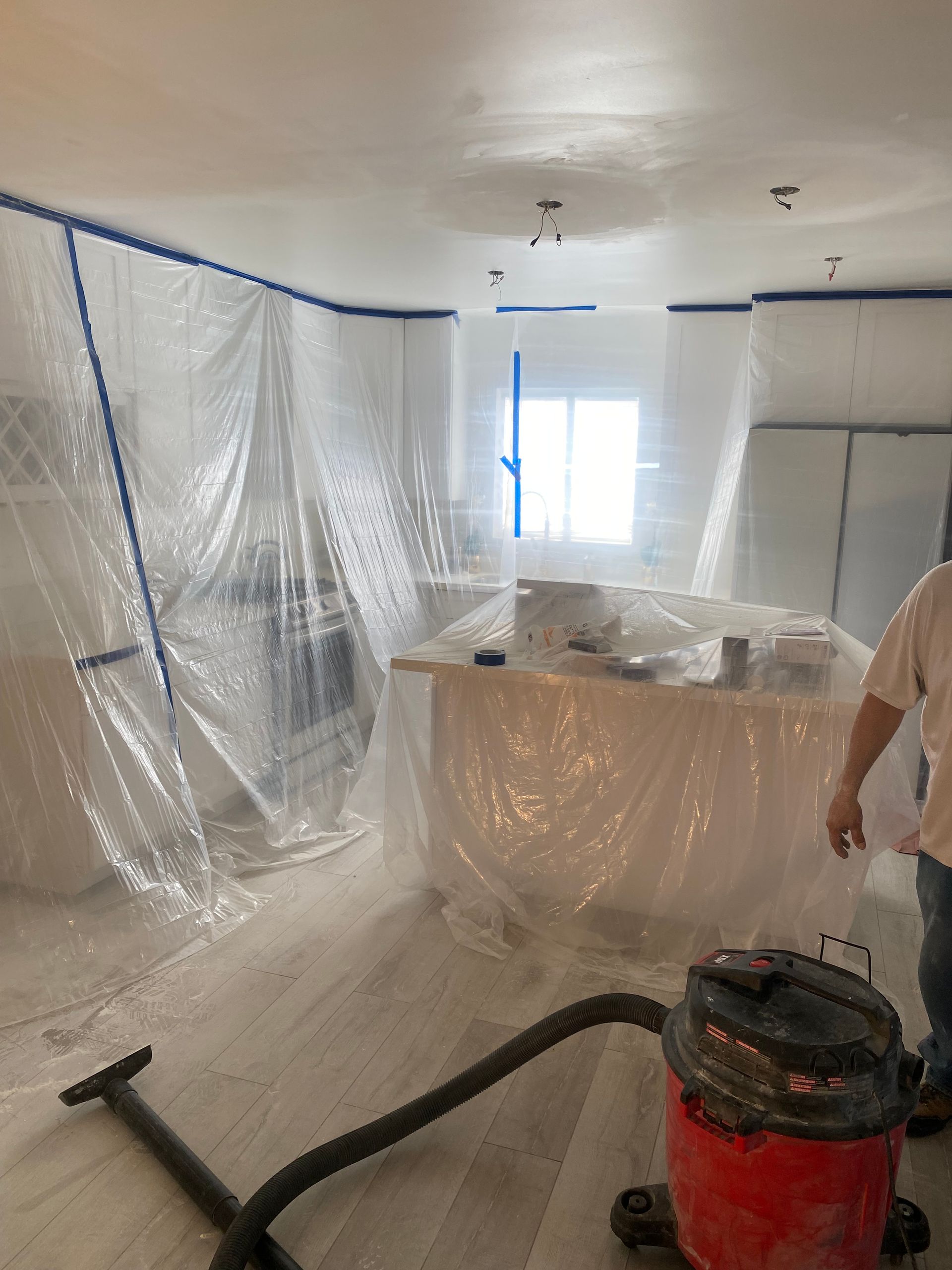 A room protected by plastic sheeting for renovation. A person and a vacuum cleaner are visible.