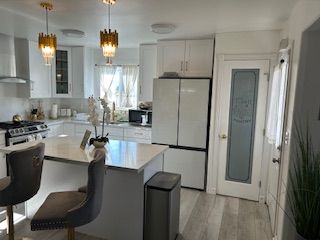 Bright kitchen with white cabinets, island, and appliances. Two pendant lights hang above the island with two gray chairs.