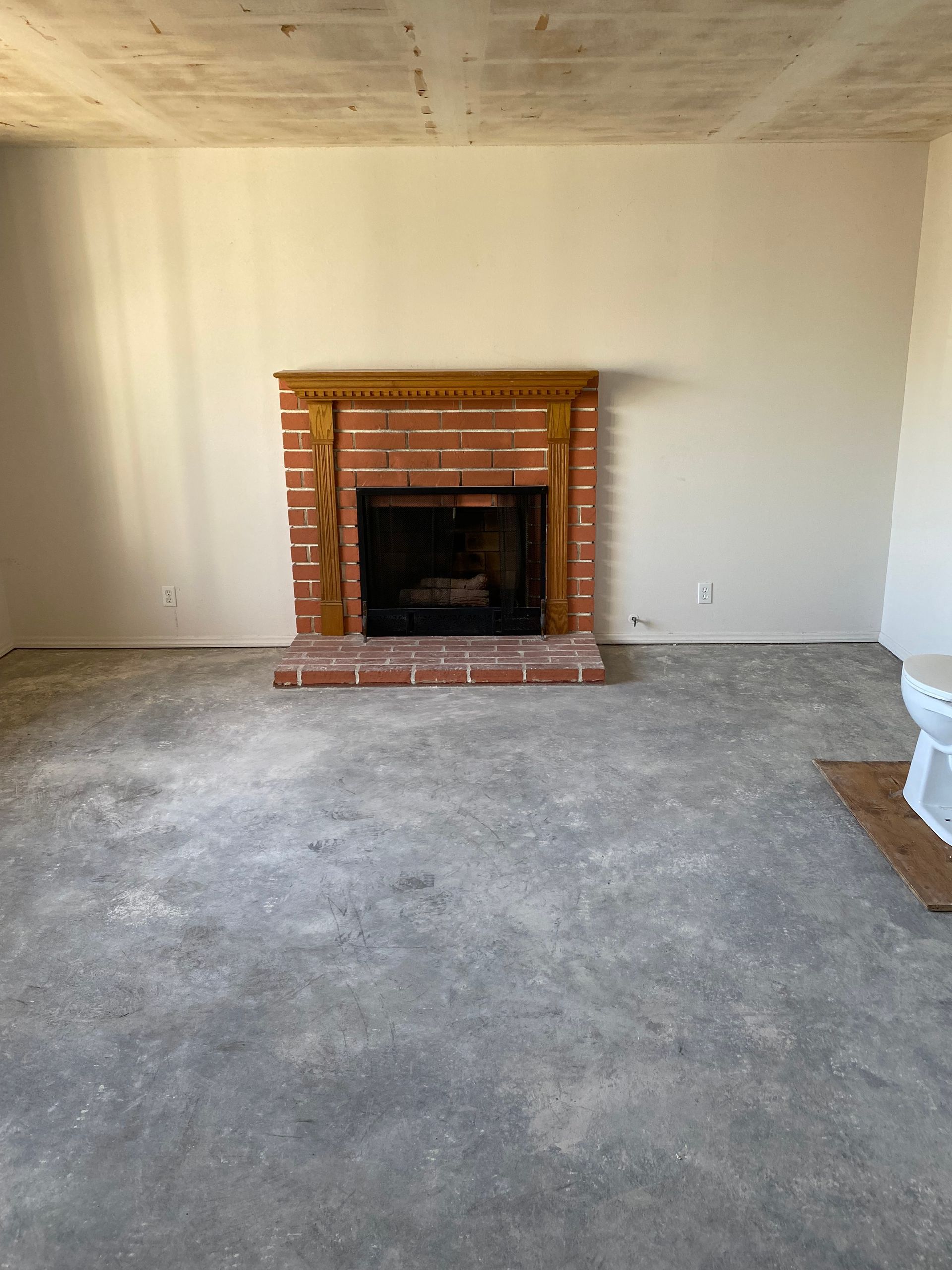 A room with a brick fireplace and wooden mantel; unfinished walls and floor.