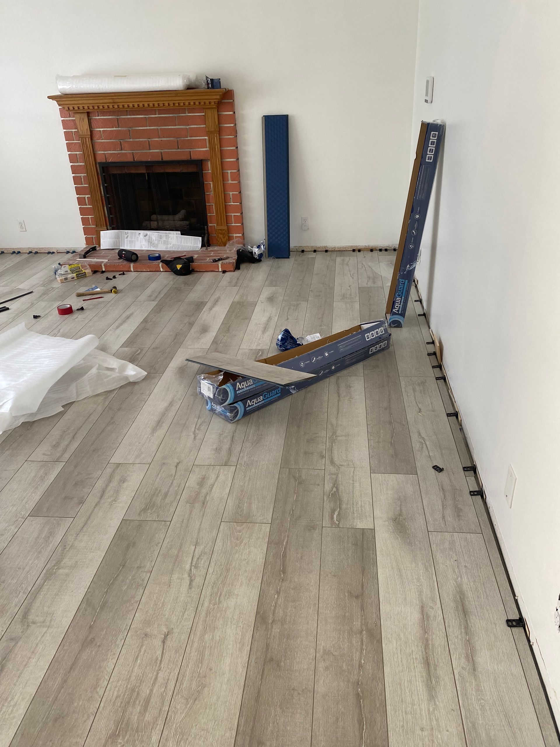 Room with fireplace, flooring boxes, and installed planks; renovation in progress.