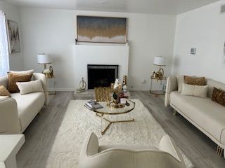 A modern living room with ivory furniture, a white fireplace, gold accents, and a fluffy rug.