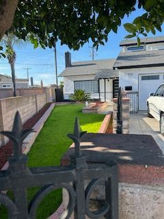 House with manicured lawn and decorative fence. White exterior, garage, and black chimney.