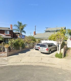 Cars parked in driveway of house with palm tree on a sunny day.