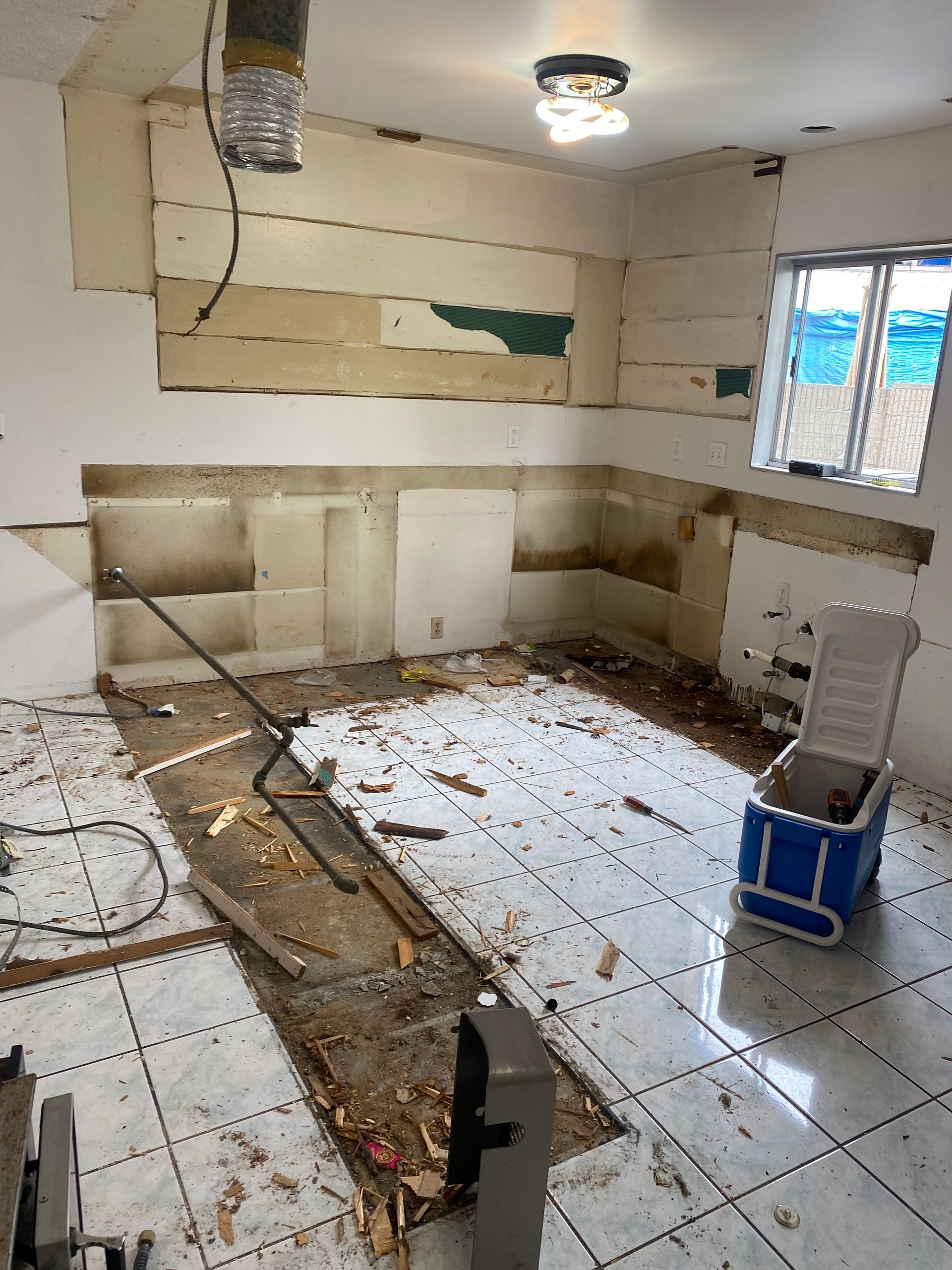 Kitchen under renovation with exposed walls and floor, debris, and a cooler.